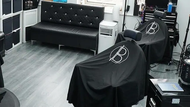 A barber chair with a PB-branded cape, the sofa behind